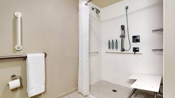 A bathroom with a shower, grab bar, toilet paper, and a shelf with toiletries.