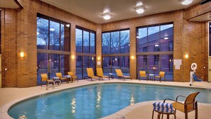 Un área de piscina con pared de ladrillo, ventanas amplias y sillones reclinables.