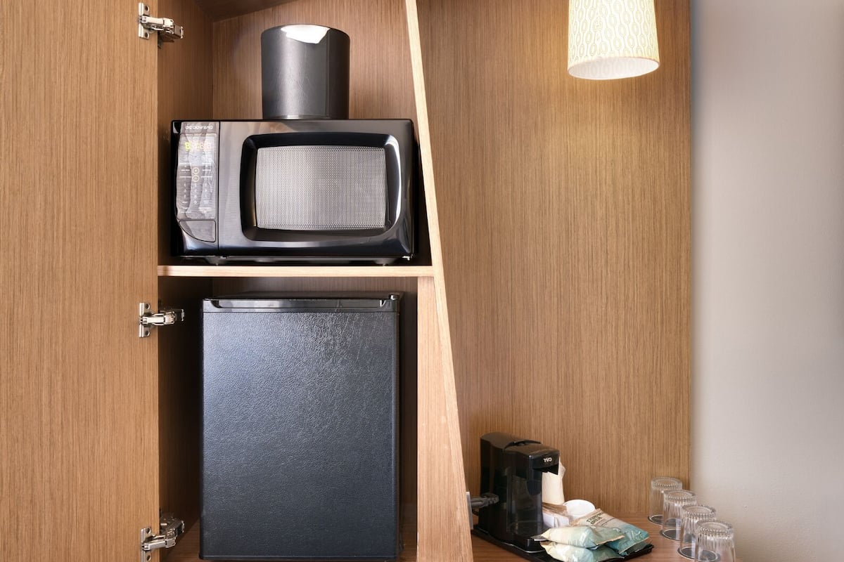 A compact kitchenette with a microwave, refrigerator, and a hanging light fixture.