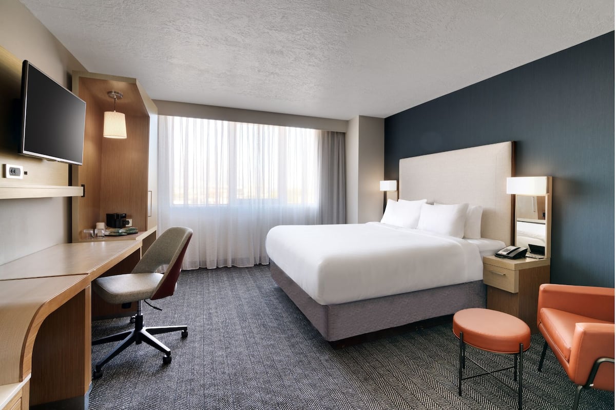 A hotel room with a bed, desk, chair, TV, and a window with curtains.