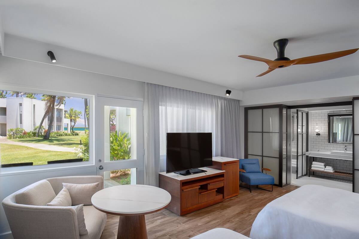 A modern hotel room with a TV, a seating area, a bed, and a view of the outdoors.