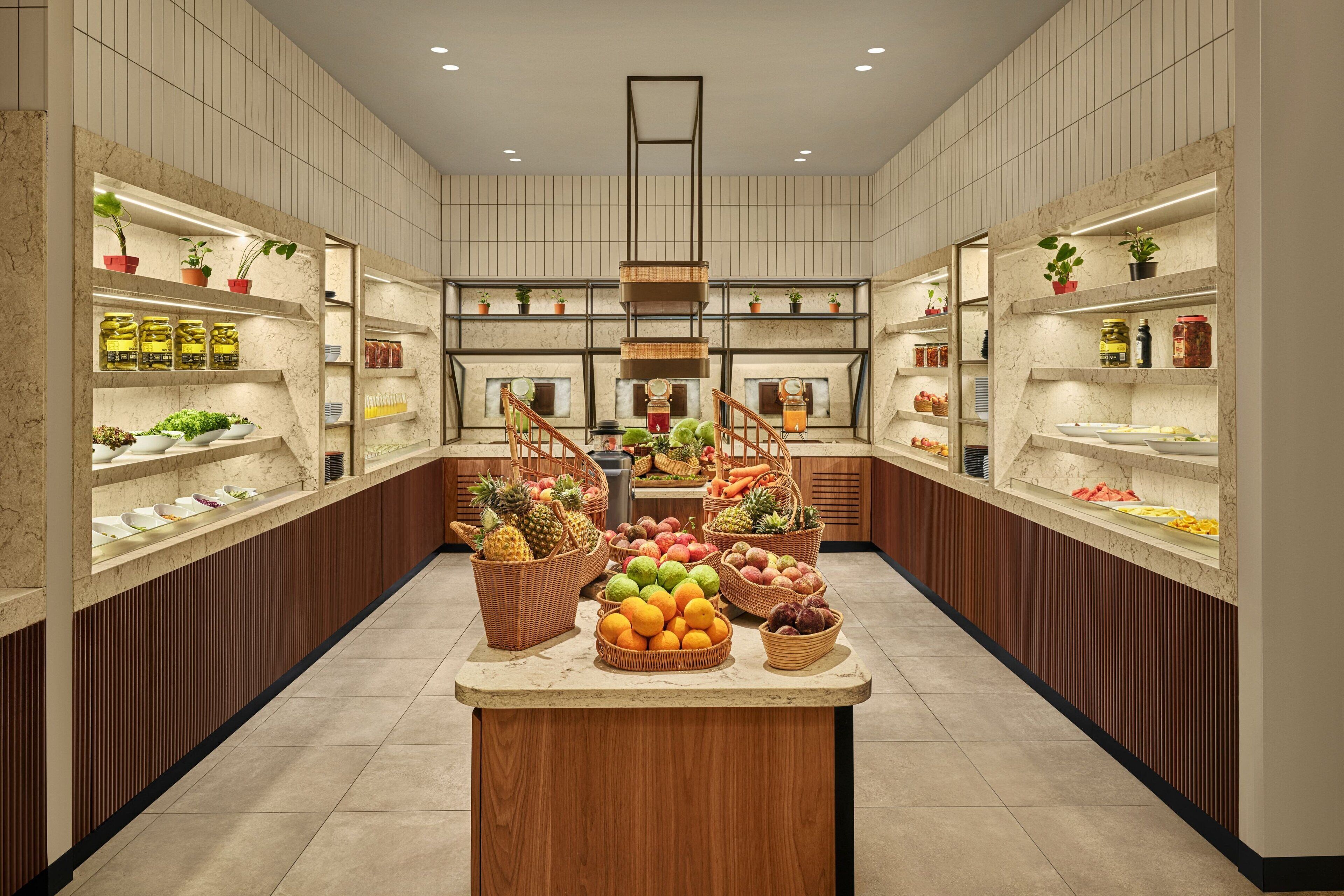 A spacious kitchen with marble countertops, wooden cabinets, and a central island with fresh produce.