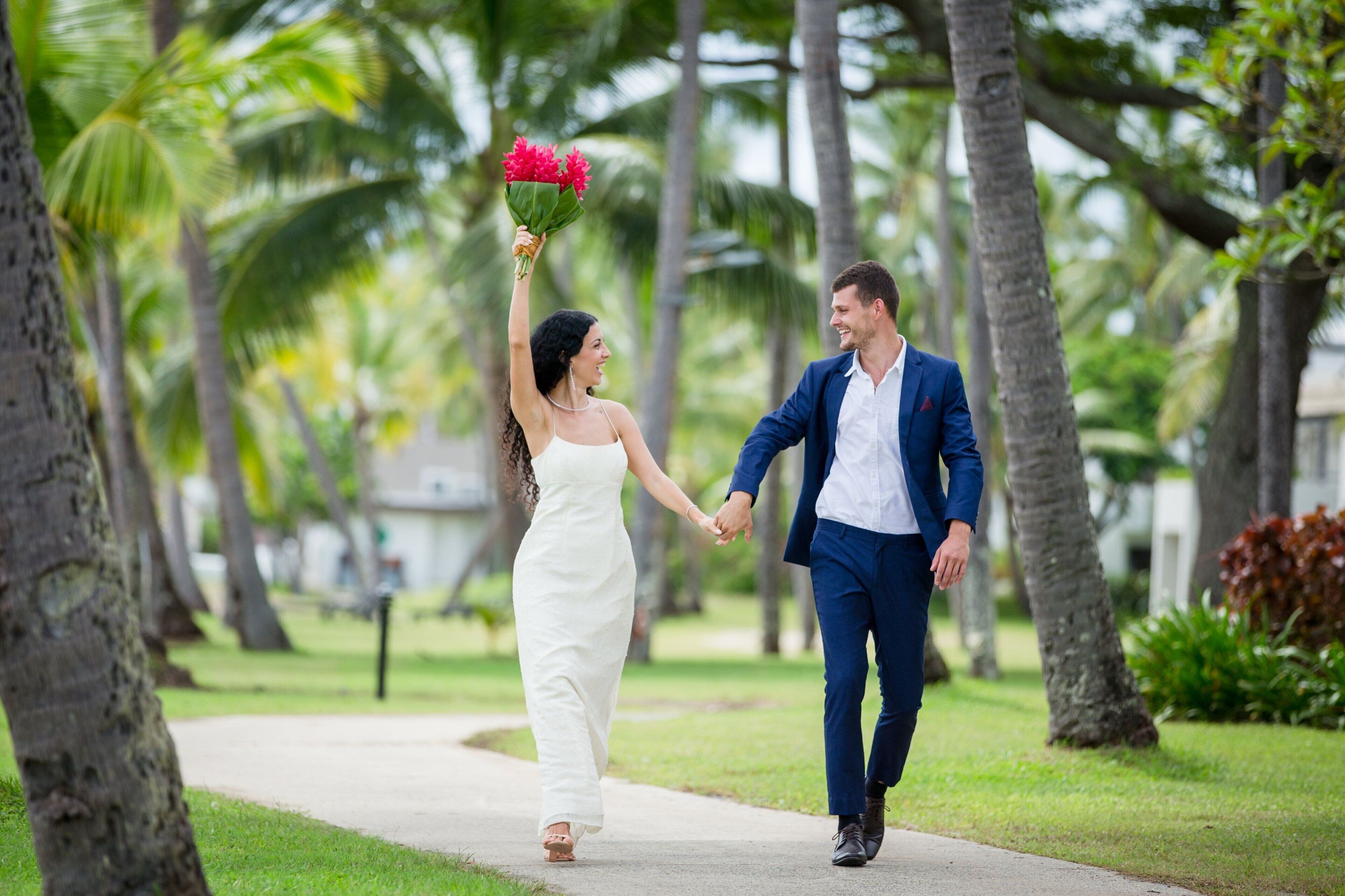 Una pareja caminando de la mano por un sendero bordeado de palmeras.
