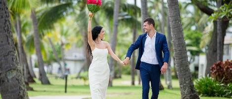 Un couple se promène, main dans la main, sur un sentier bordé de palmiers.