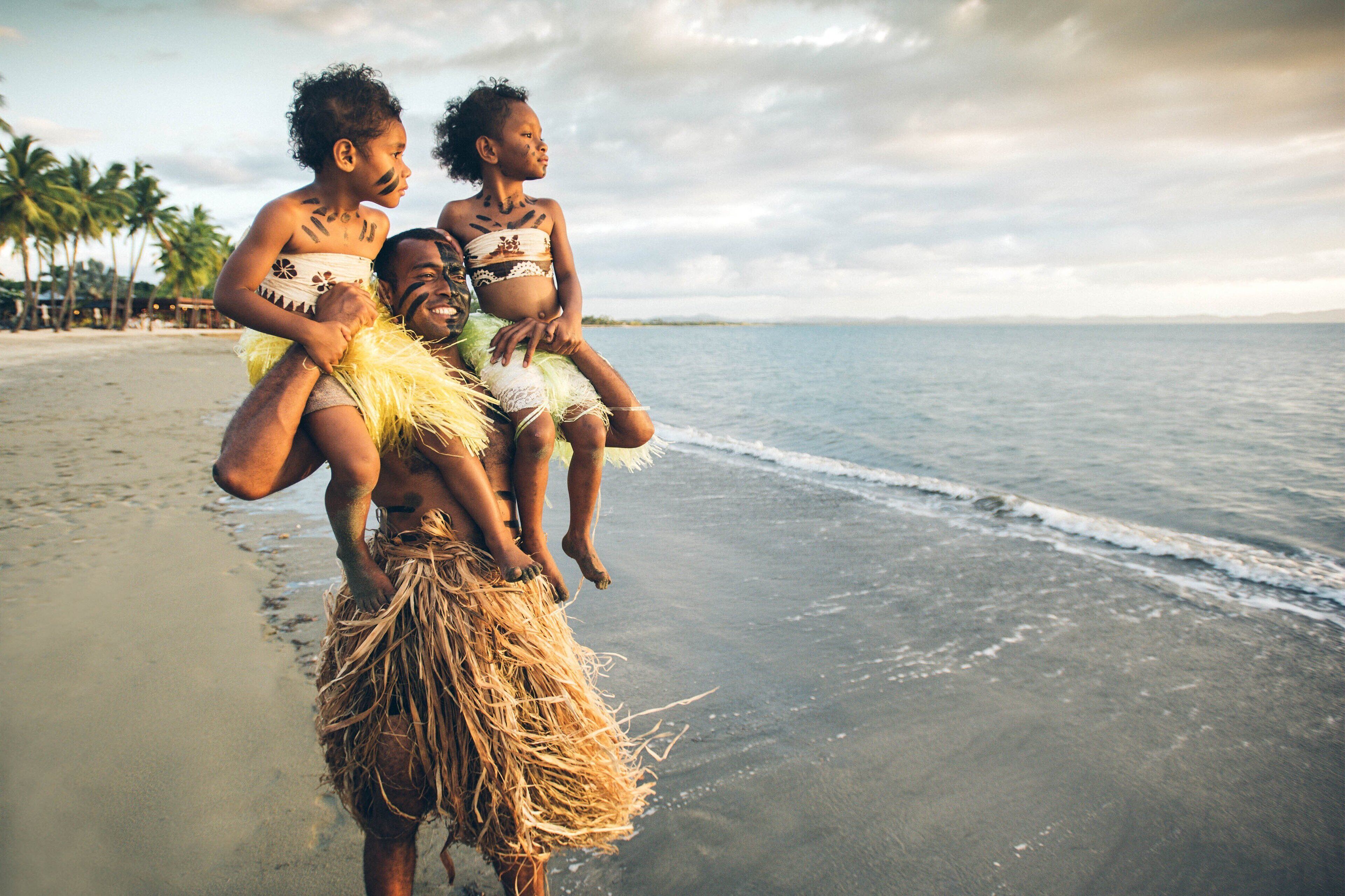 A beach scene with a person carrying two children on their shoulders.