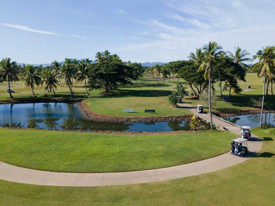 A golf course with a pond, palm trees, and a clear sky.