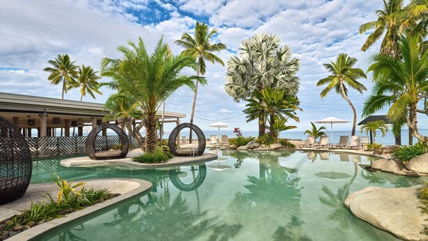 A resort pool area with palm trees, lounge chairs, and a view of the ocean. - Sheraton Fiji Golf & Beach Resort (Nadi)