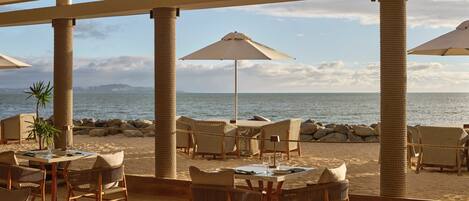 A beachside patio with wicker furniture and umbrellas, overlooking the sea.