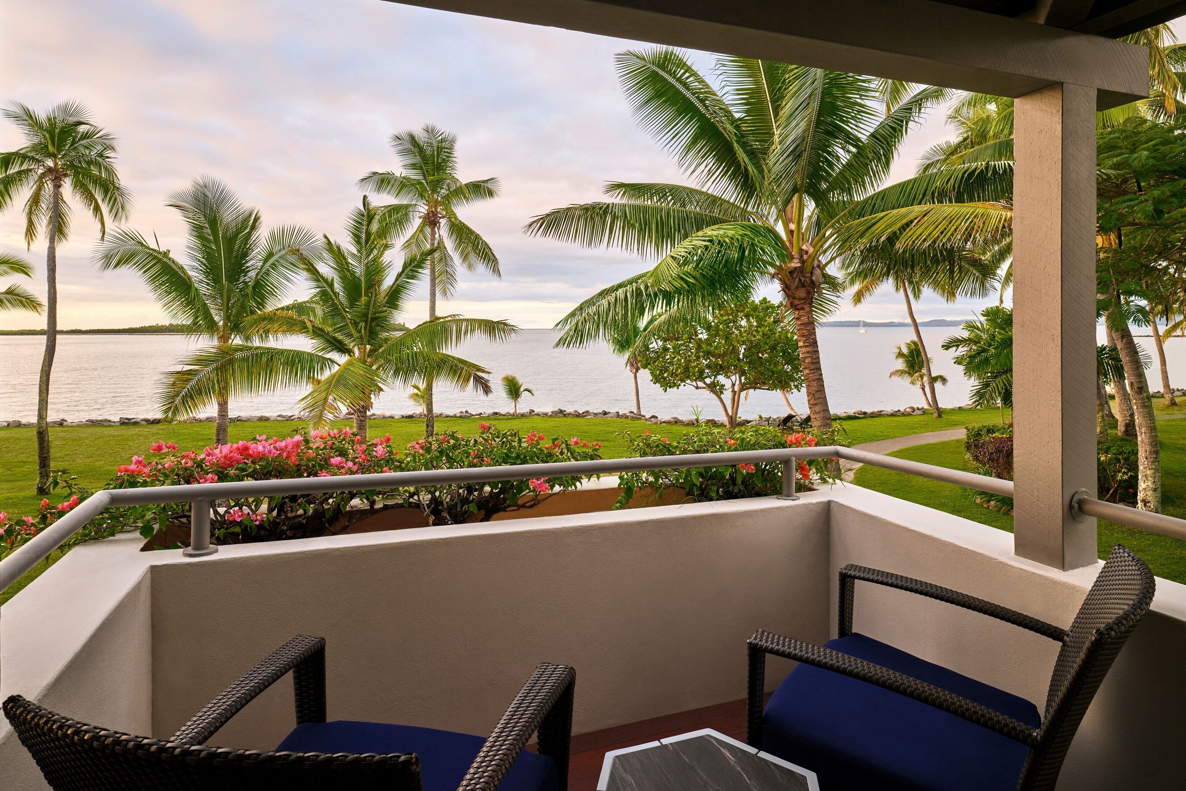 A balcony with wicker furniture and a view of the sea and palm trees.