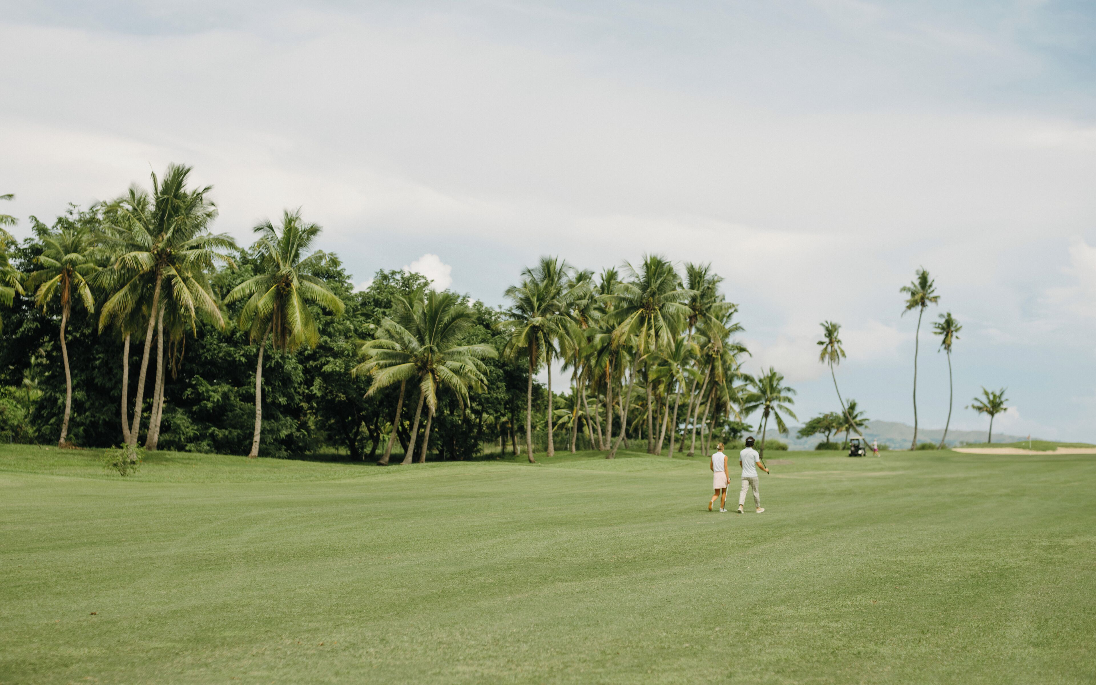 Un campo de golf con un césped bien cuidado, palmeras y cielo despejado.