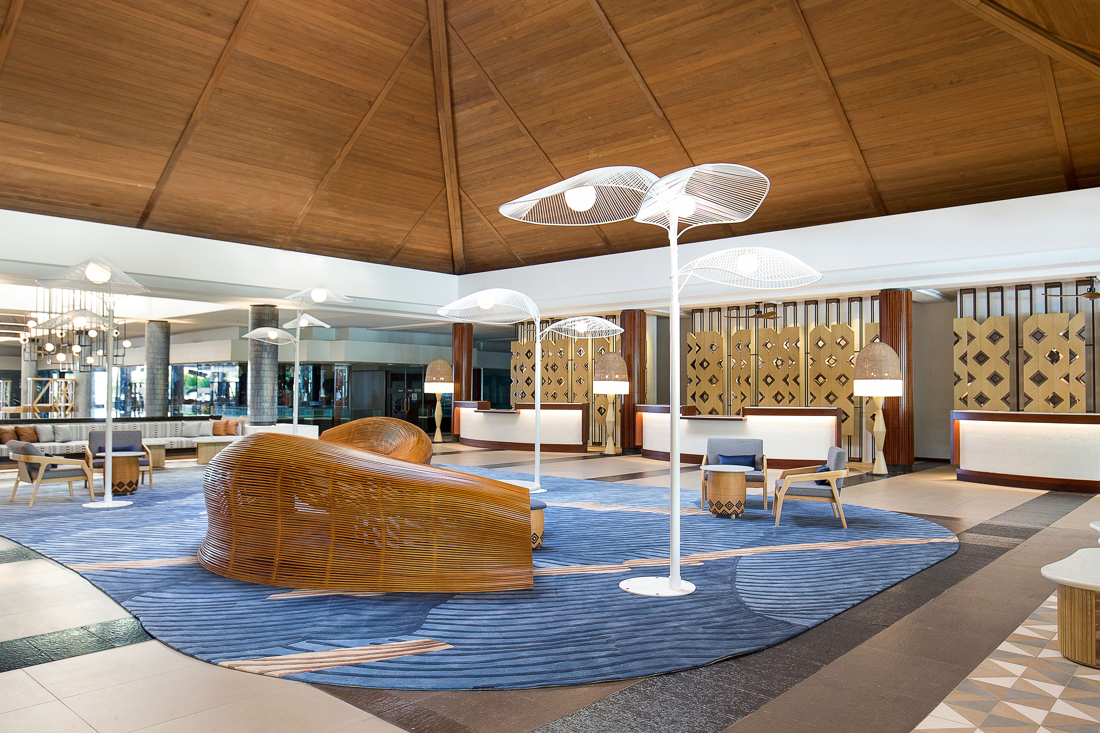 A spacious lobby with a high ceiling, a reception desk, seating areas, and decorative lighting.