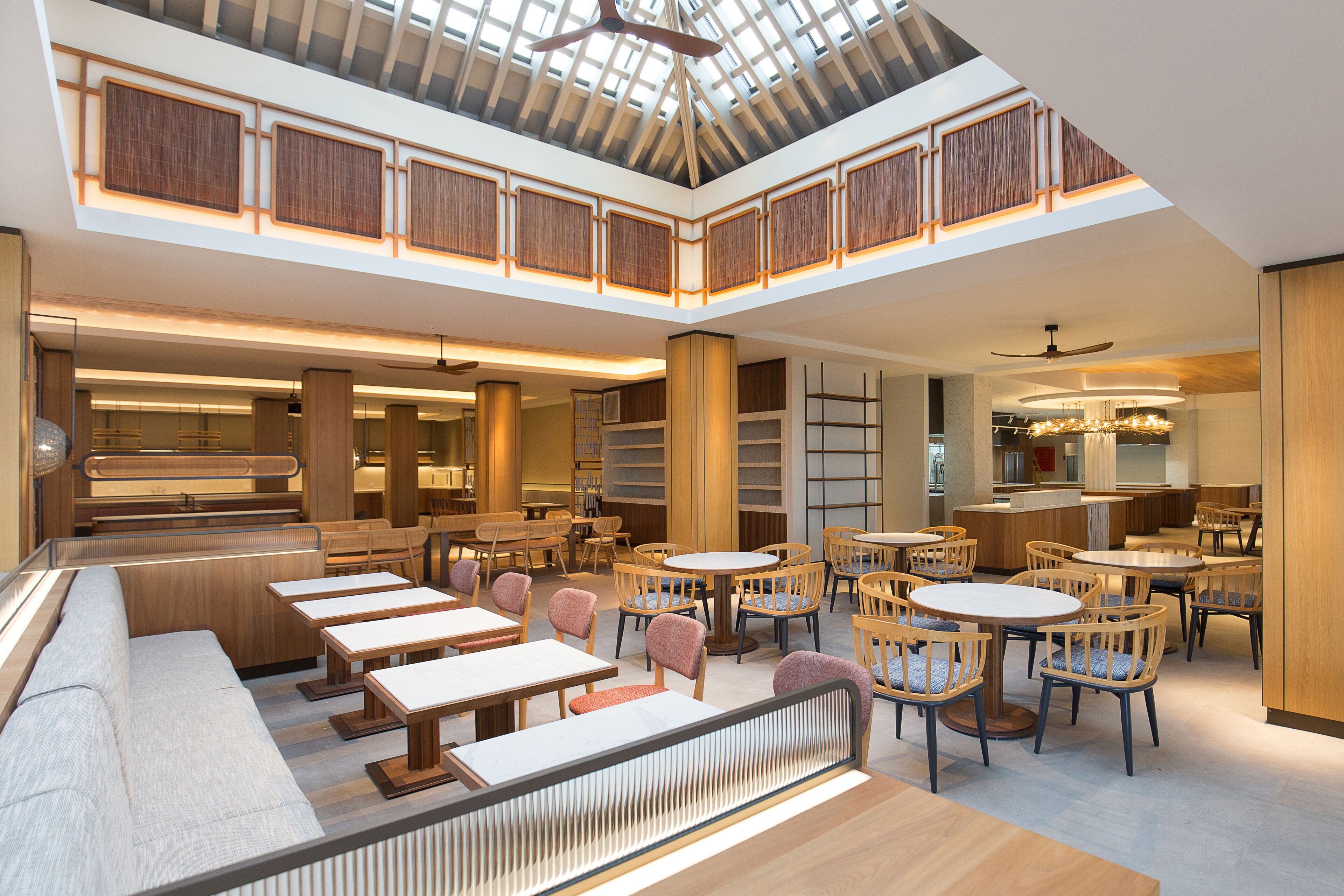 A spacious indoor area with multiple seating arrangements, including tables and chairs, and a high ceiling with a skylight.