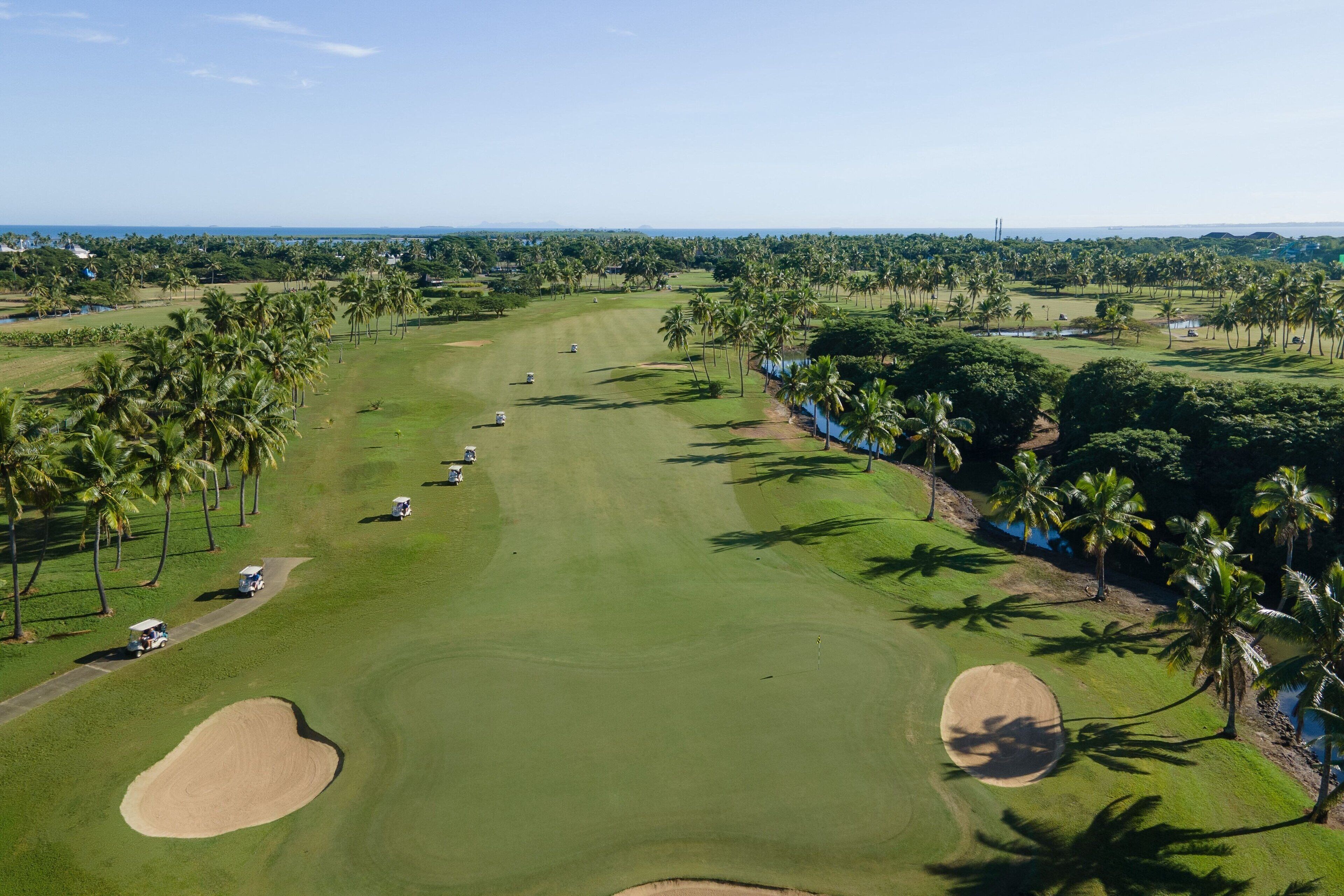A golf course with bunkers, palm trees, and a clear sky.