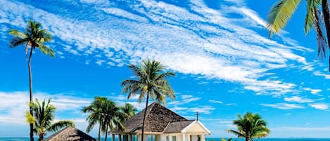 A beachside chapel with a white exterior, surrounded by palm trees and a clear blue sky.