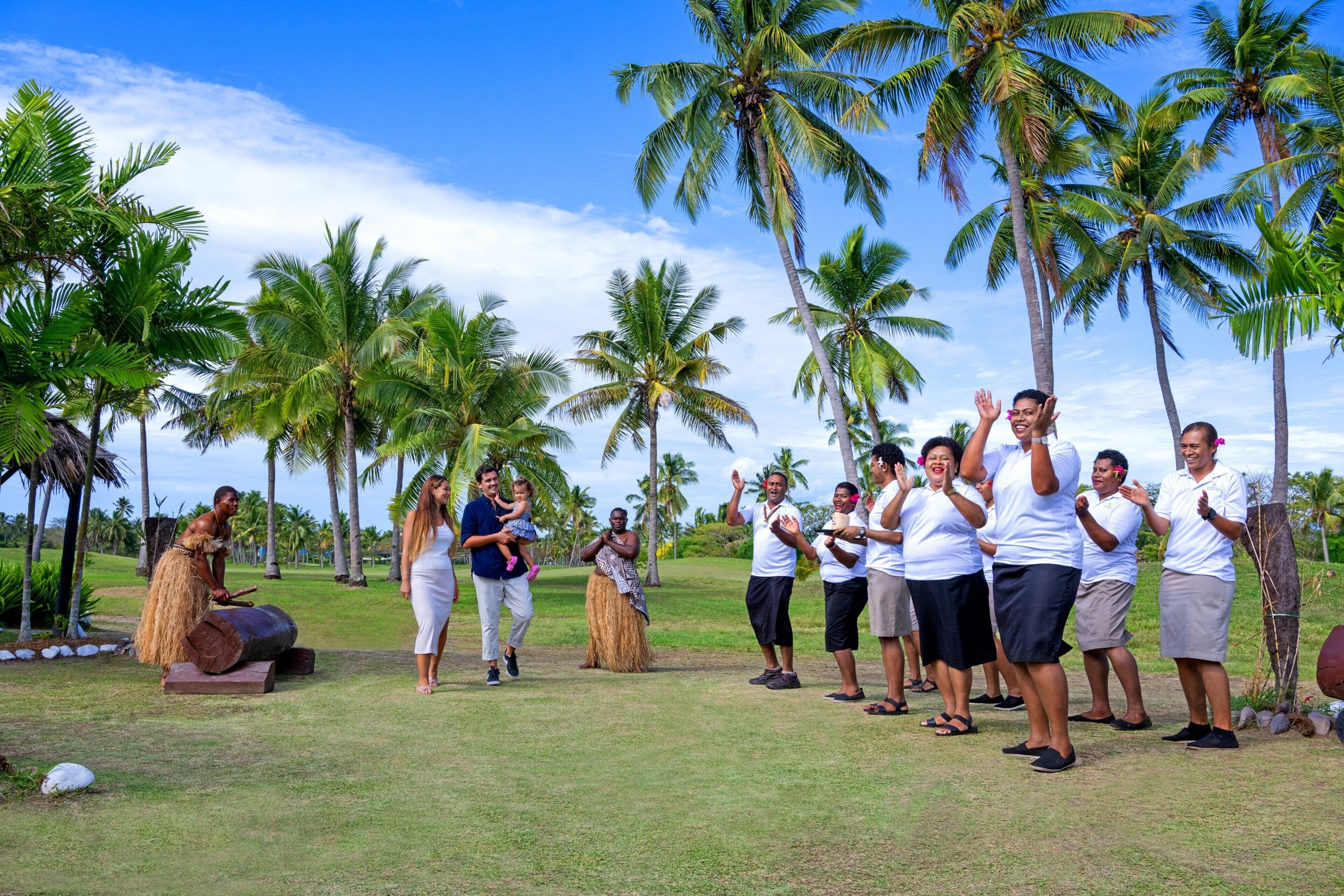 A group of people outdoors with palm trees in the background.