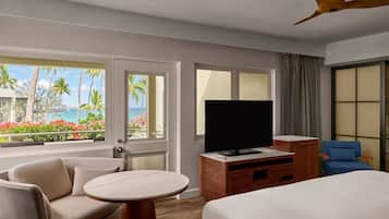 Een hotelkamer met een bed, een televisie, een bureau, een stoel en uitzicht op zee.