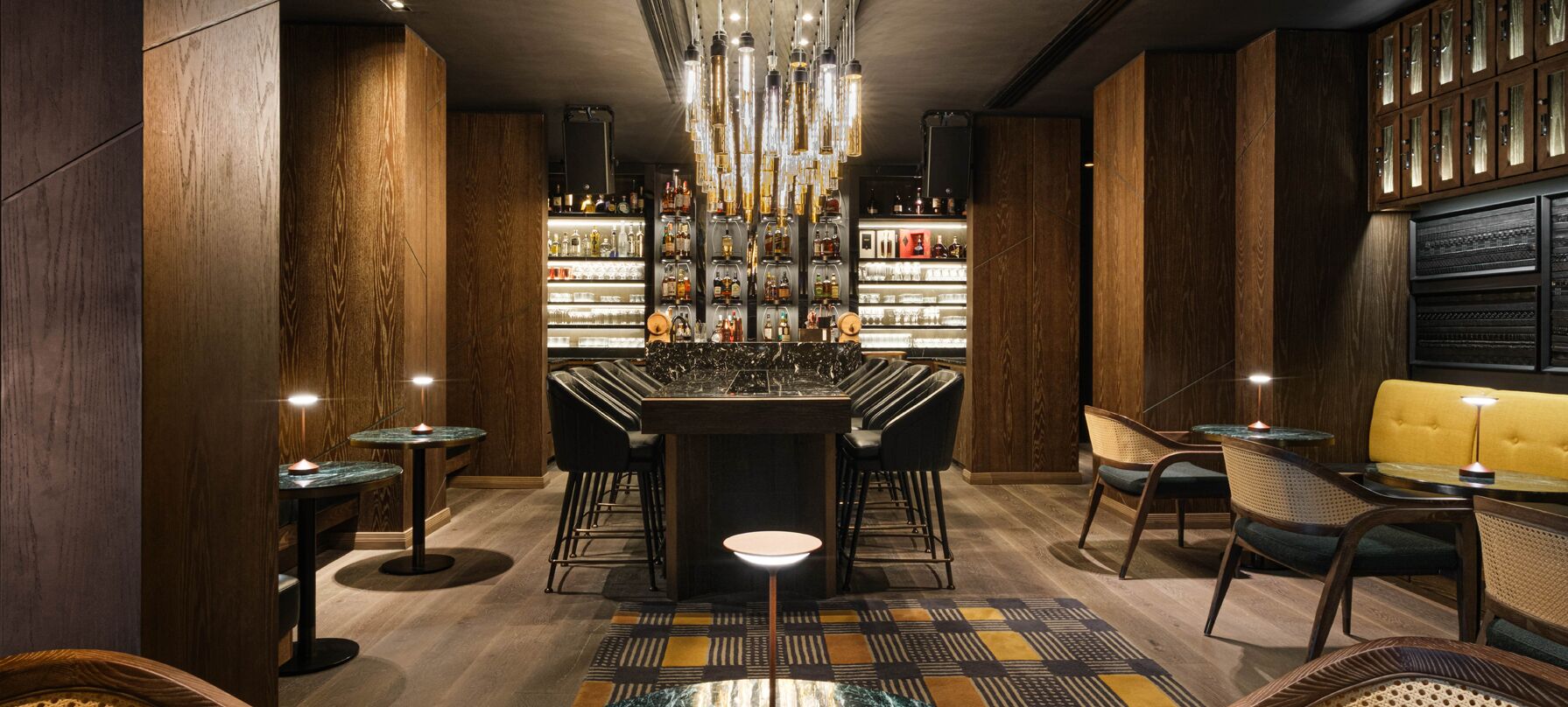 A bar area with a central bar, multiple seating options, and a well-stocked liquor shelf.