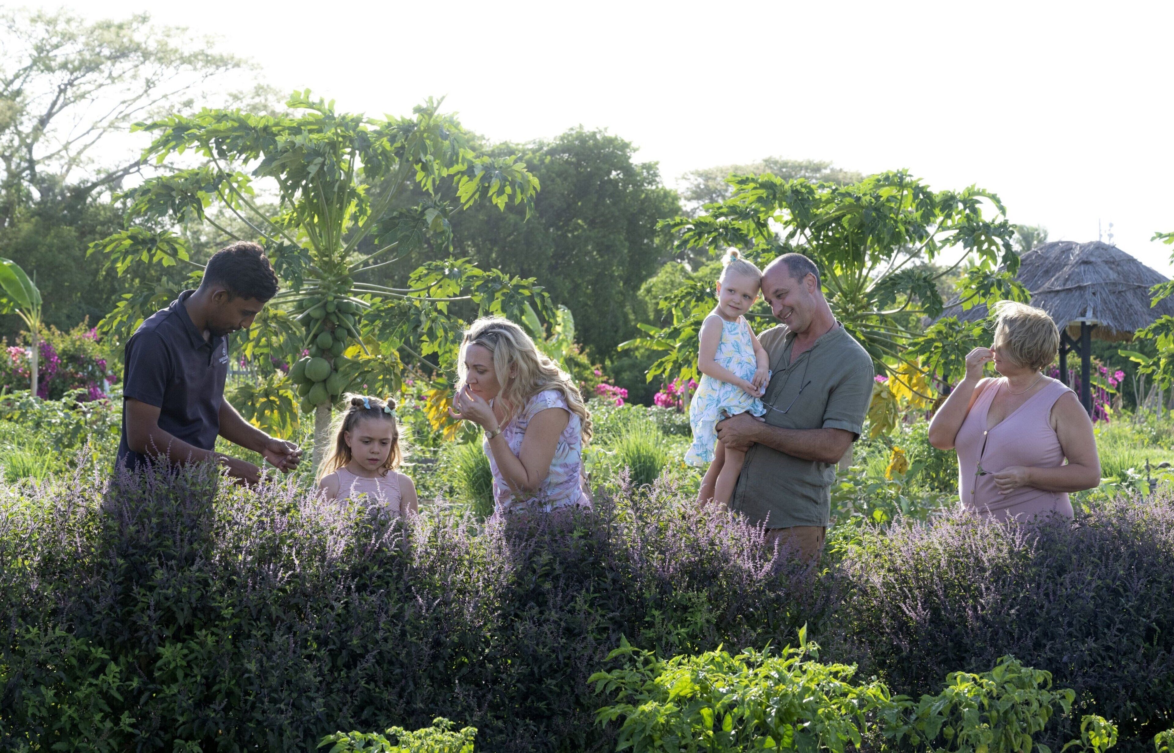 A family in a garden with lush greenery and a thatched-roof structure.