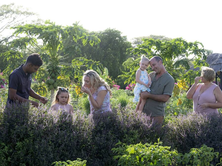 A family in a garden with lush greenery and a thatched-roof structure.