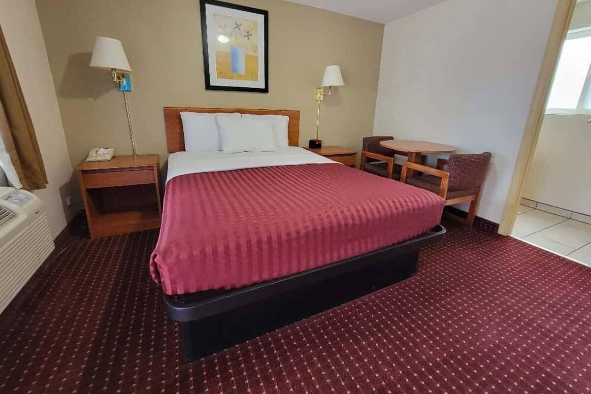 A hotel room with a bed, a desk, two lamps, and a framed picture on the wall.