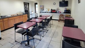 A restaurant with multiple tables and chairs, a kitchen area, and a television mounted on the wall. - Americas Best Value Inn Williams Grand Canyon (Williams)