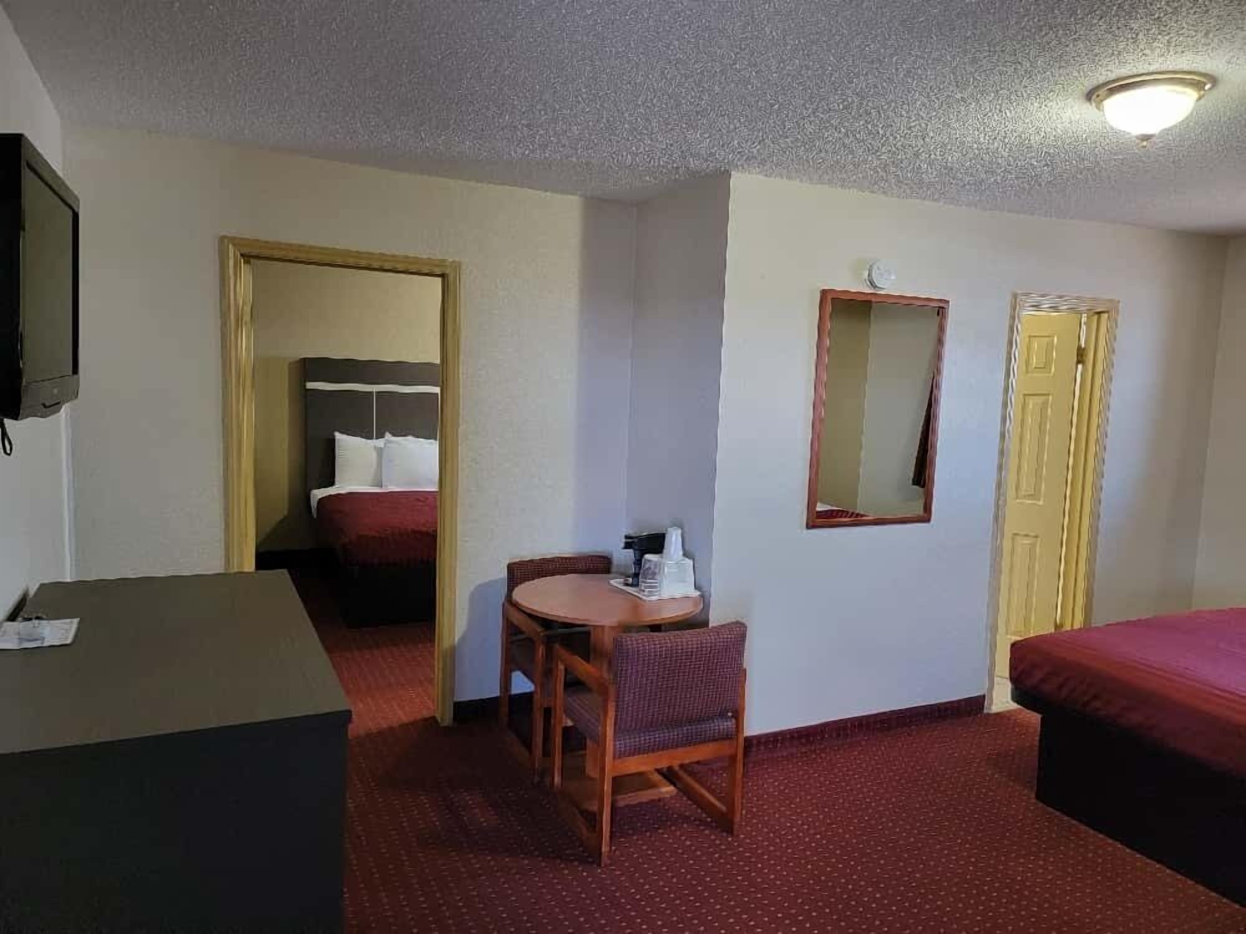A hotel room with a bed, a desk, a chair, a small table, a mirror, and a wardrobe.