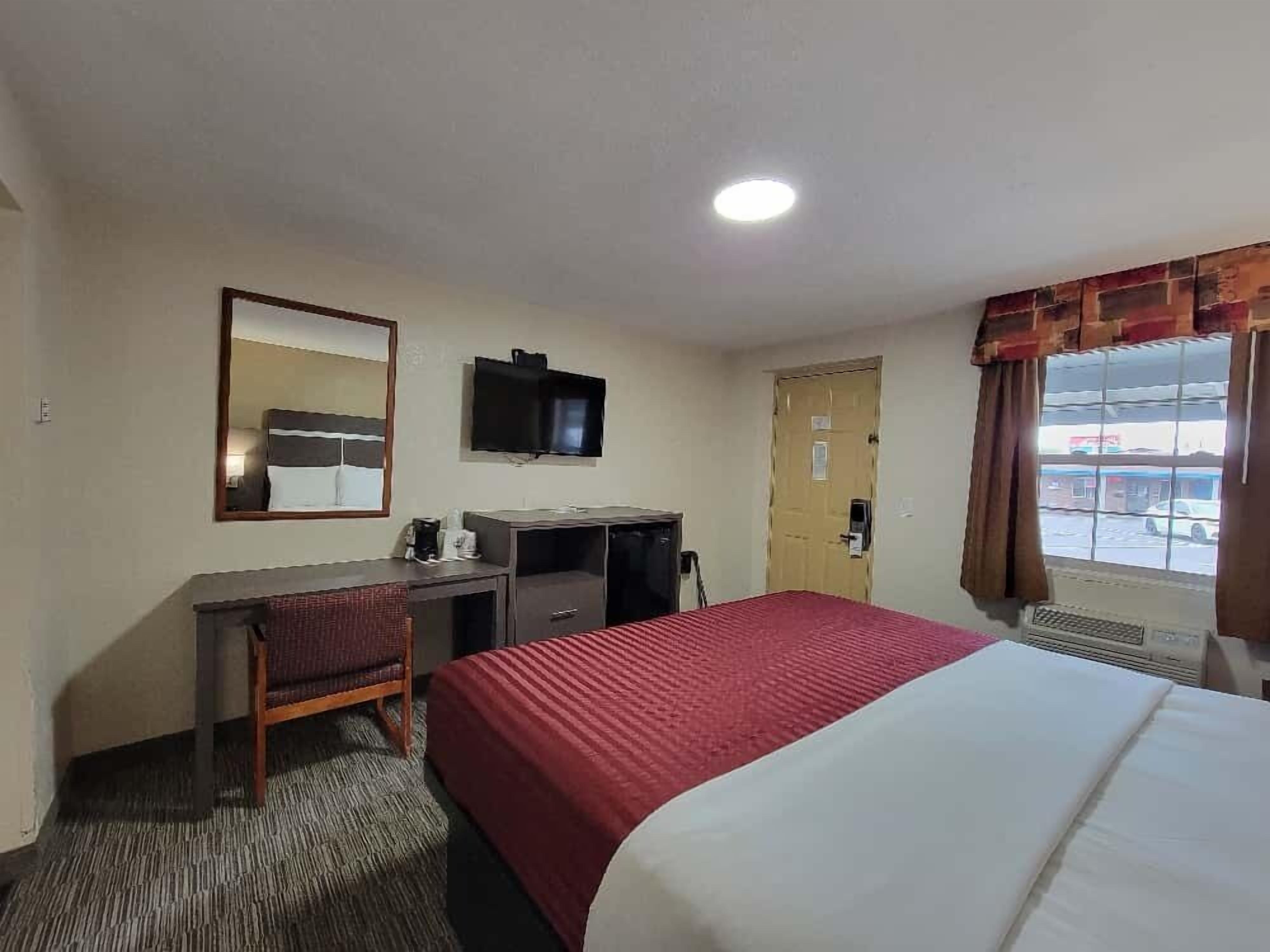 Habitación de hotel con cama, escritorio, silla, televisor y ventana con cortinas.