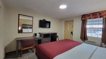 Habitación de hotel con cama, escritorio, silla, televisor y ventana con cortinas.