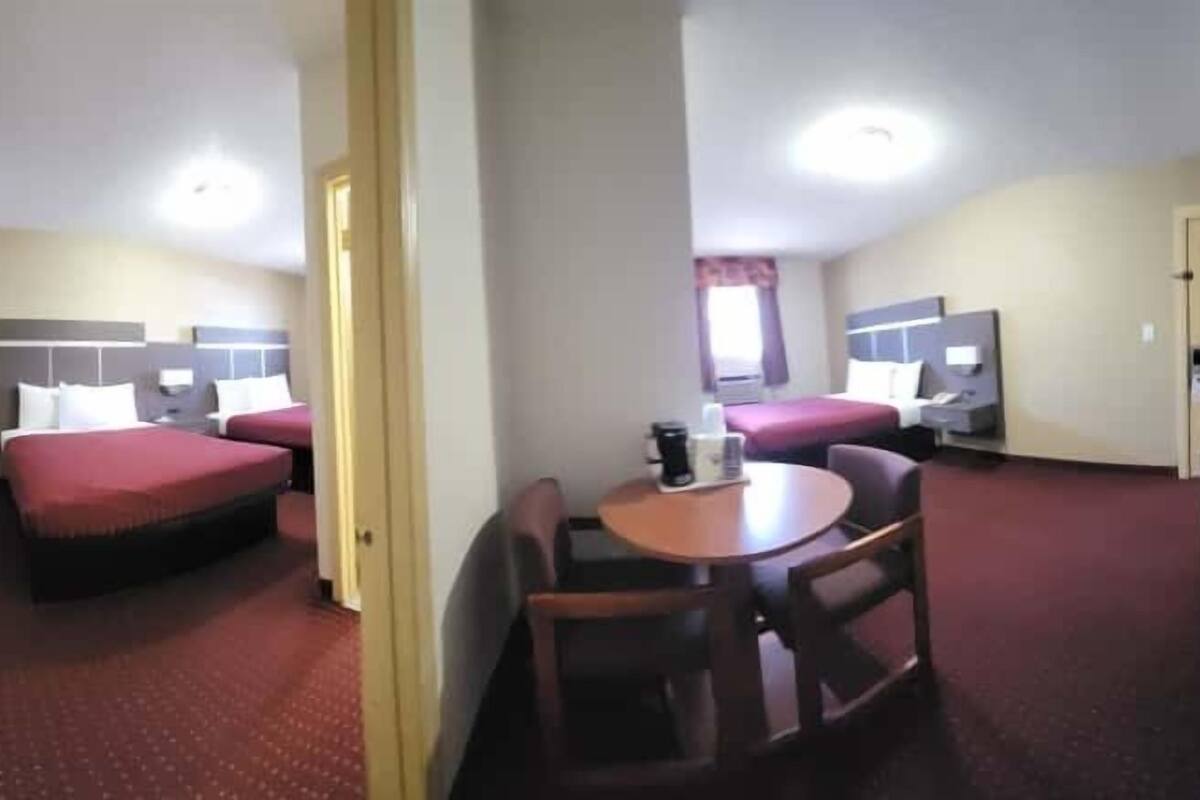 A hotel room with two beds, a small table, a chair, and a desk with a computer.