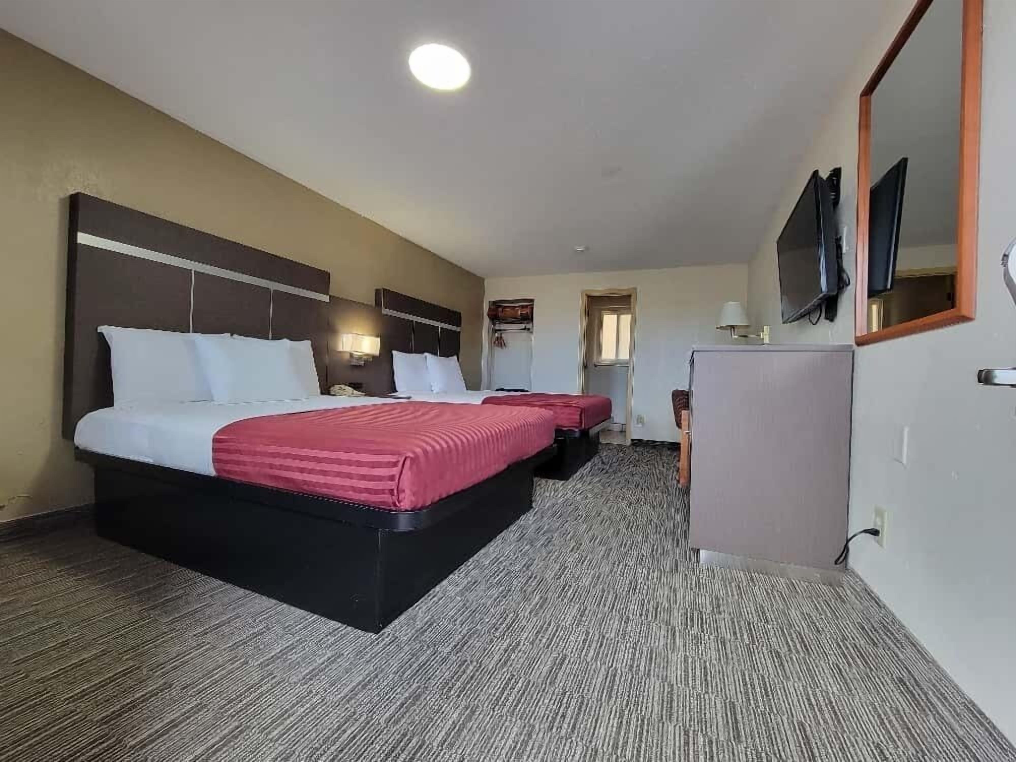 A hotel room with two beds, a desk, a television, and a mirror.