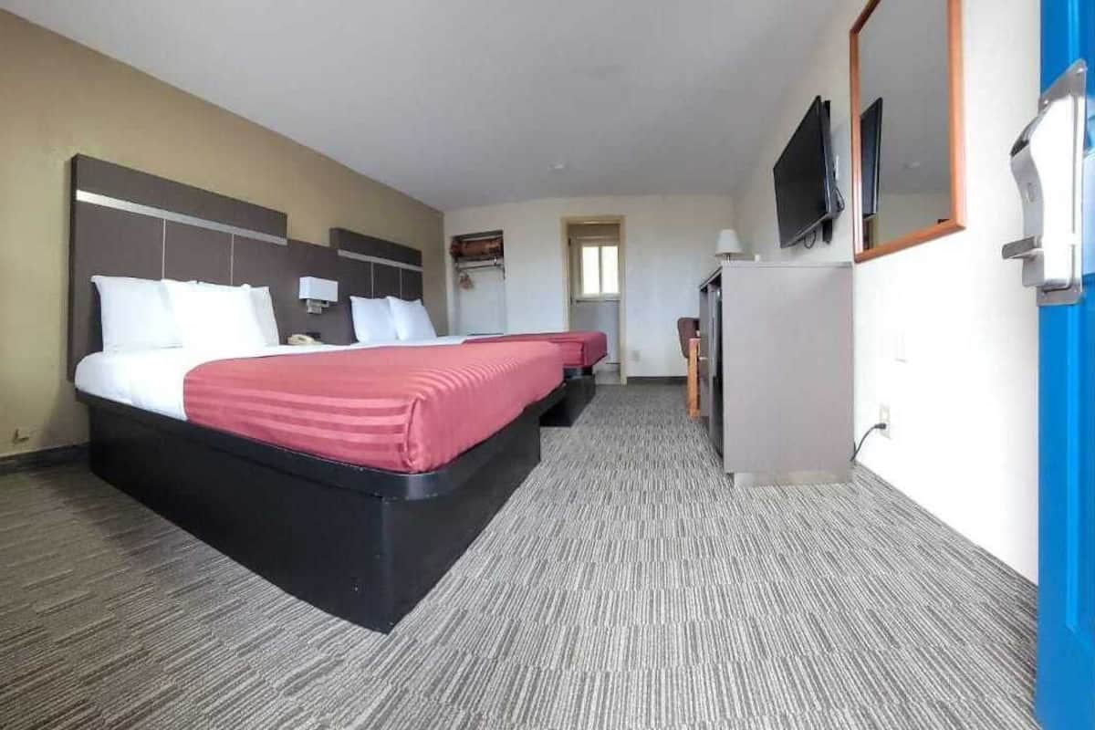 A hotel room with a large bed, a desk, a chair, a television, and a mirror.