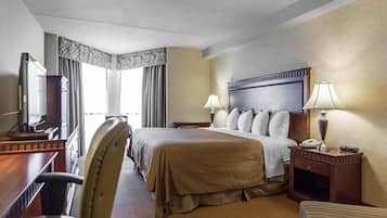 Une chambre d’hôtel comprenant un lit, un bureau avec une télévision, une chaise, une table de chevet avec une lampe et une fenêtre avec des rideaux.