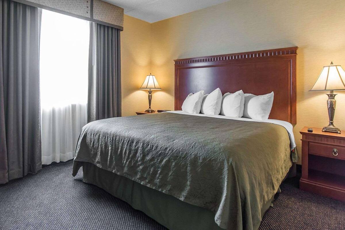 Une chambre d’hôtel avec un grand lit, deux tables de chevet avec des lampes, une tête de lit en bois et une fenêtre avec des rideaux.