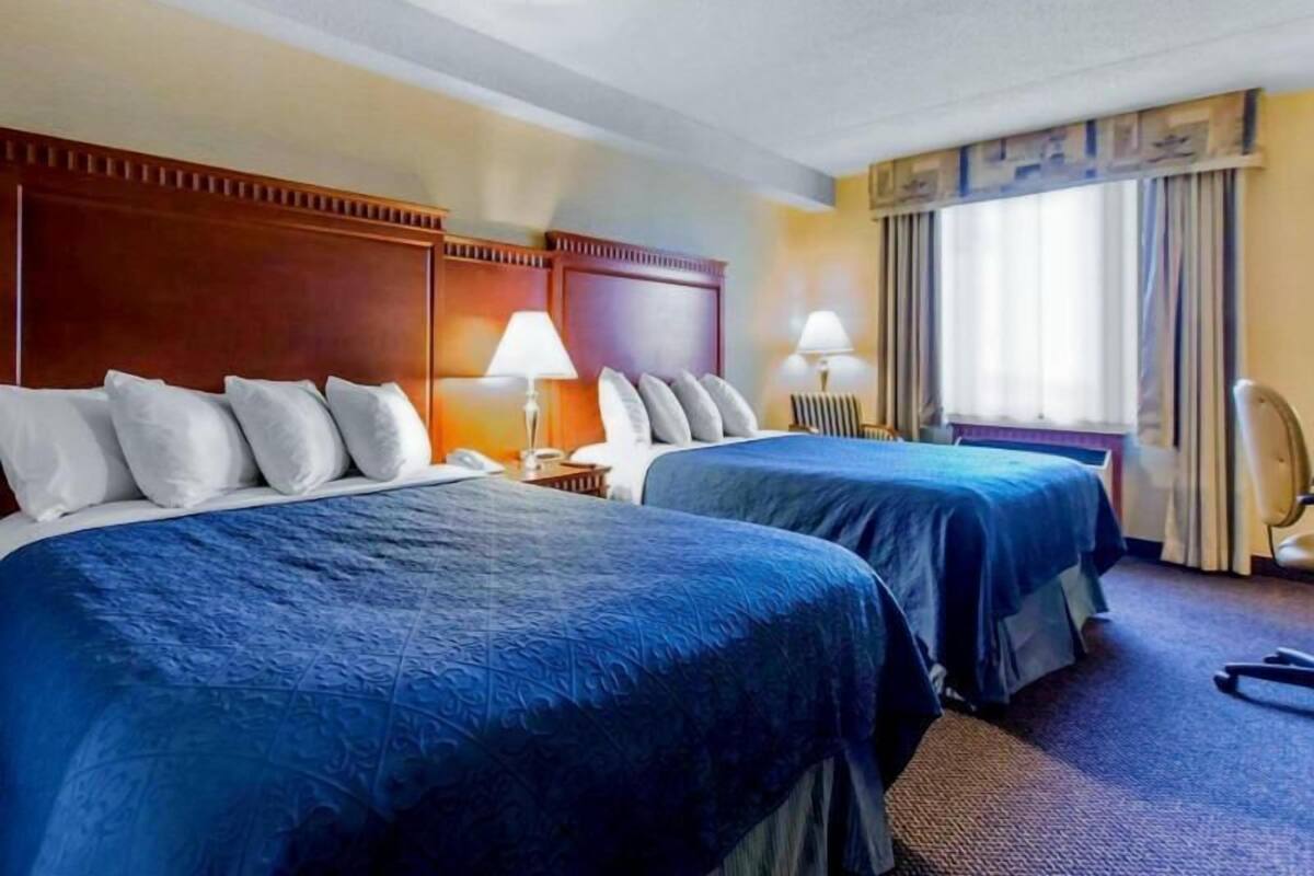 Une chambre d’hôtel avec deux lits, une tête de lit en bois, un bureau et une chaise.