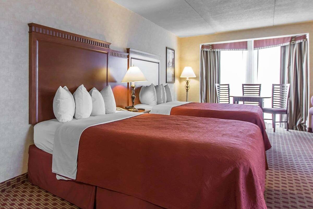 Une chambre d’hôtel avec deux lits, un coin salon avec une table et des chaises, et une vue sur l’extérieur.