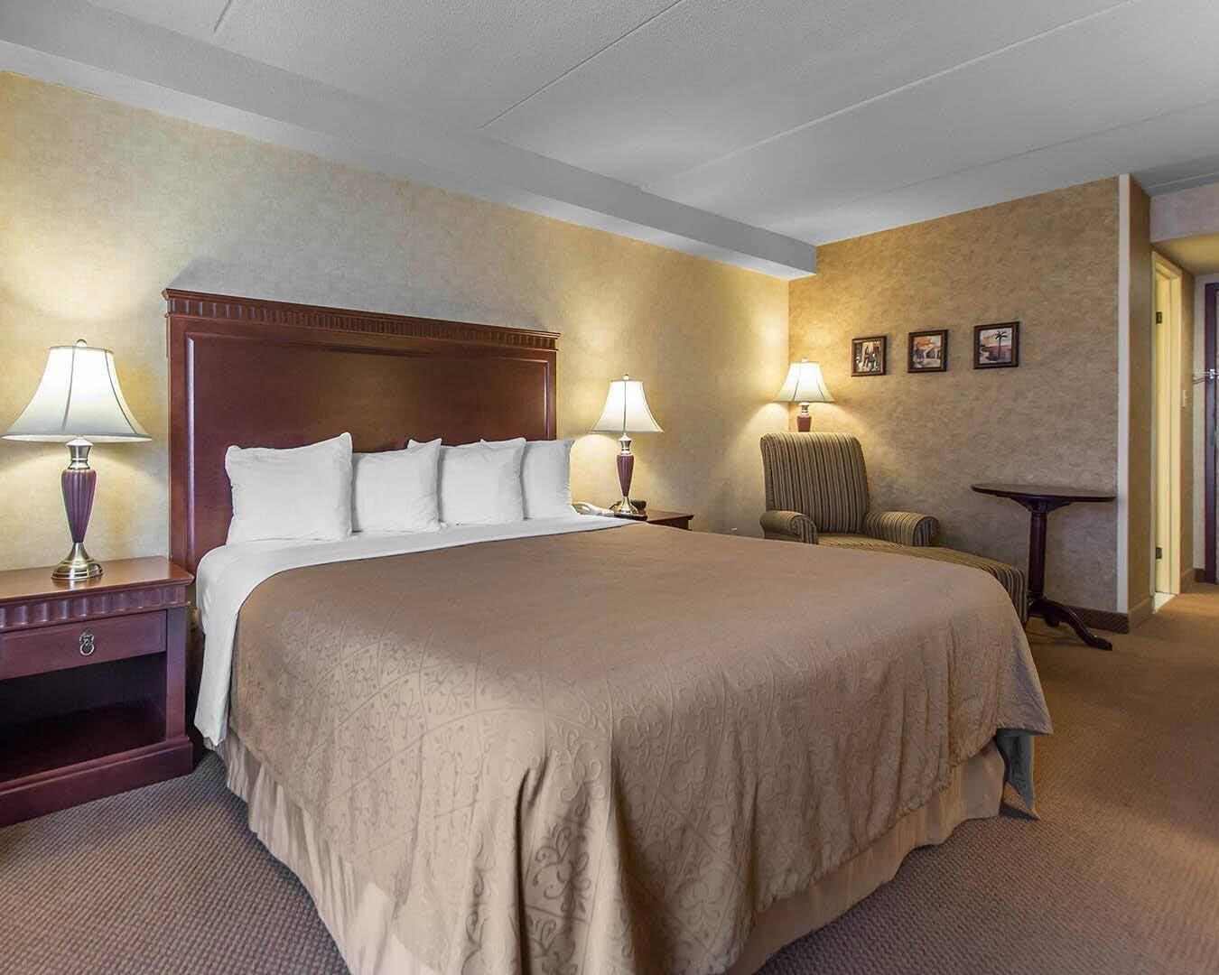 Una habitación de hotel con una cama grande, dos mesitas de noche con lámparas, una silla y una mesita pequeña.