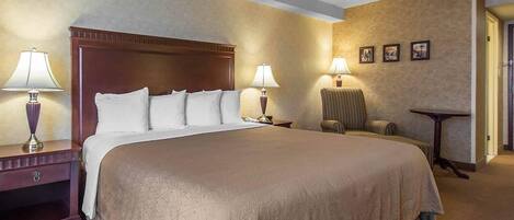 Una habitación de hotel con una cama grande, dos mesitas de noche con lámparas, una silla y una mesita pequeña.
