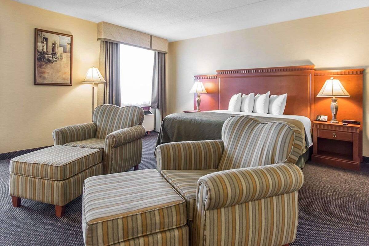 Une chambre d’hôtel comprenant un lit, deux fauteuils, une petite table et une table de chevet avec une lampe.