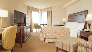 Habitación de hotel con cama, escritorio con televisor, silla, mesita de noche con lámpara y un reposapiés a rayas.