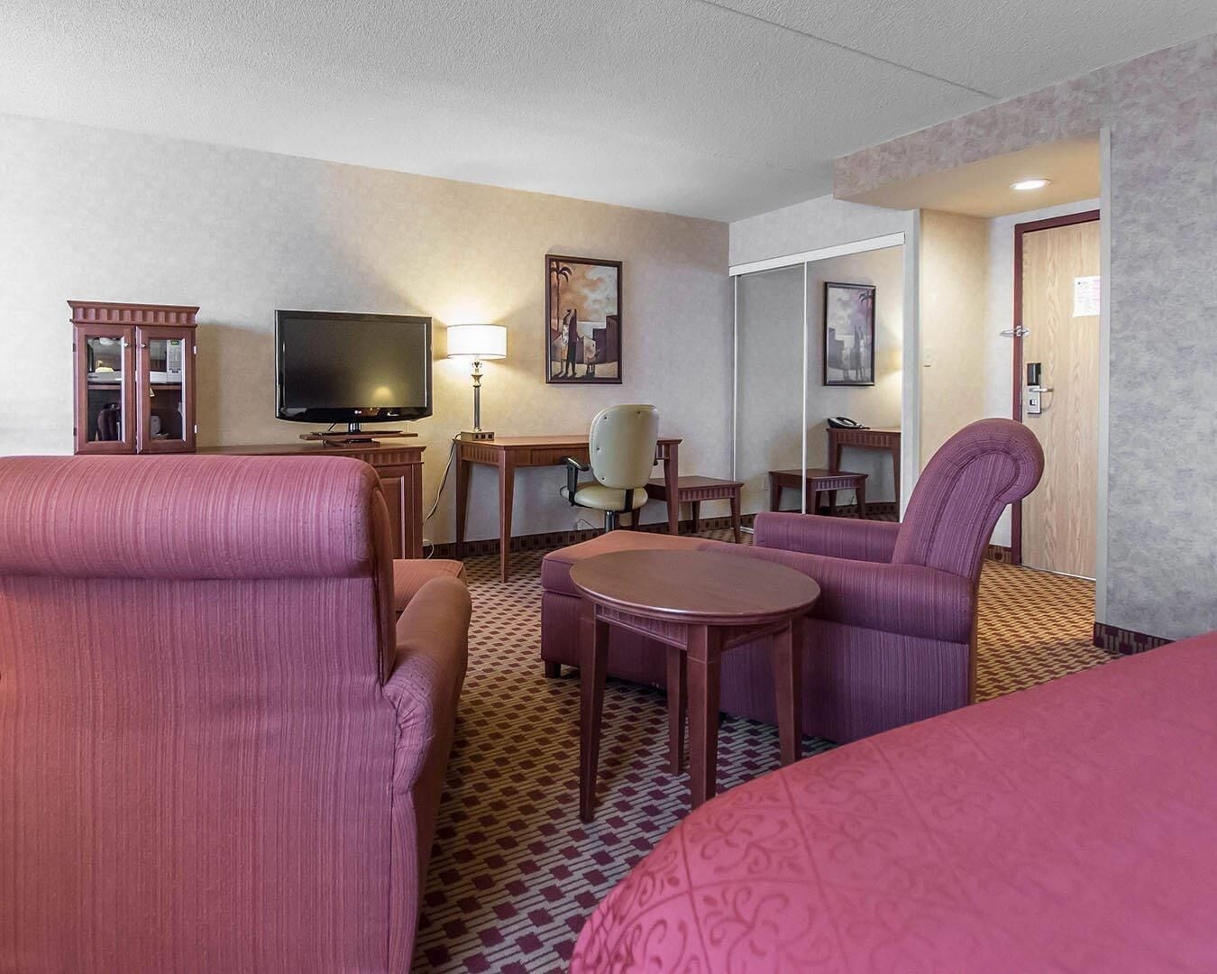 A hotel room with a bed, two armchairs, a desk, a television, and a lamp.