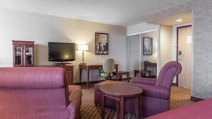 Una habitación de hotel con una cama, dos sillones, un escritorio, un televisor y una lámpara.
