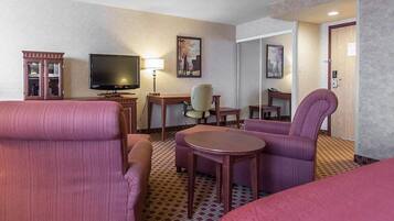 A hotel room with a bed, two armchairs, a desk, a television, and a lamp.