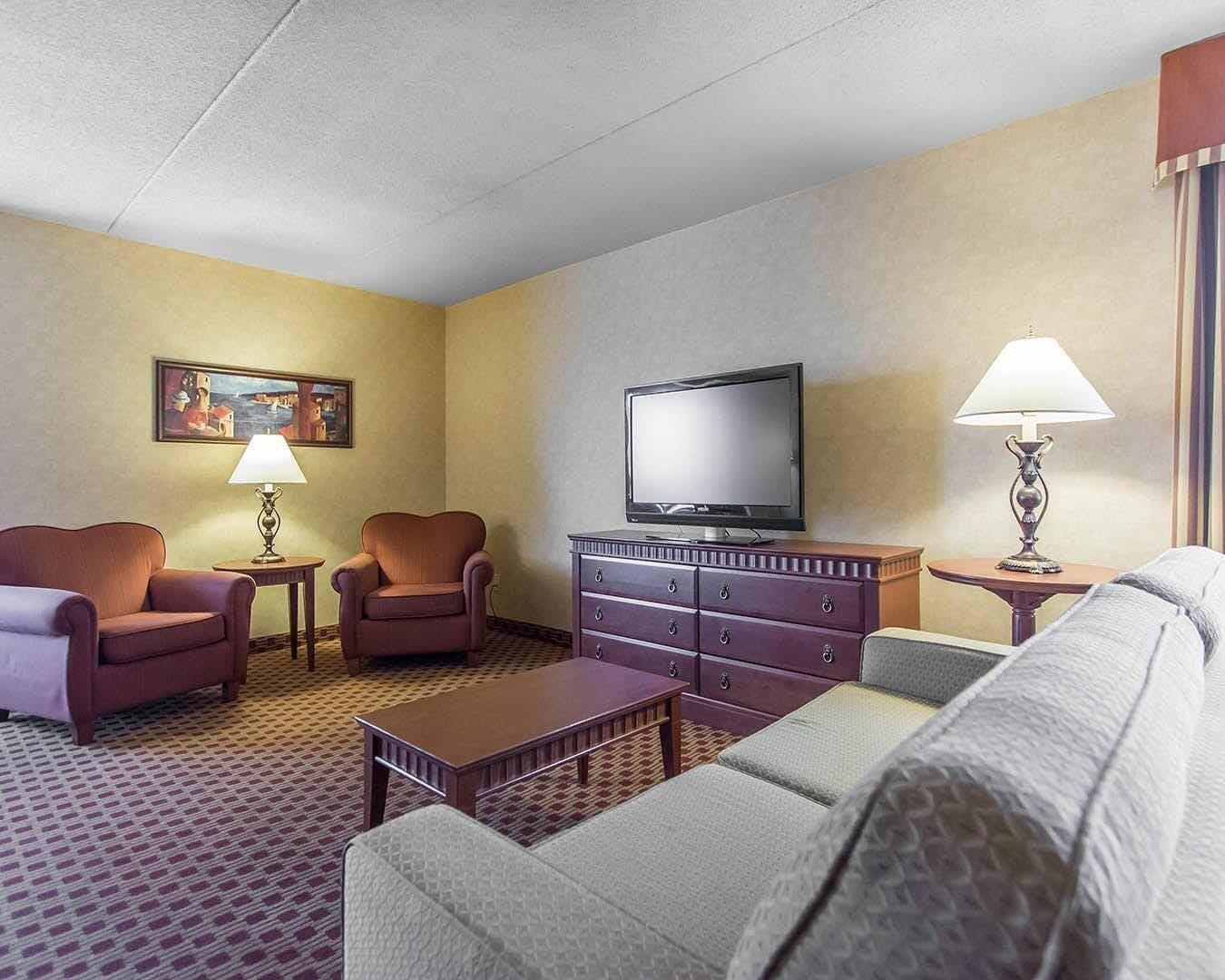 Habitación de hotel con sofá, dos sillones, televisor, lámpara y un cuadro en la pared.