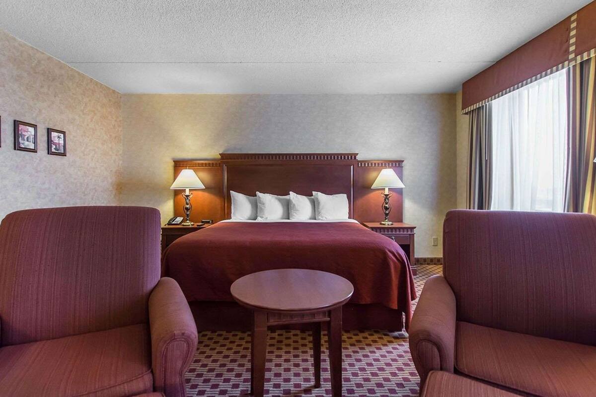 Une chambre d’hôtel avec un grand lit, deux lampes de chevet, une petite table et deux fauteuils.