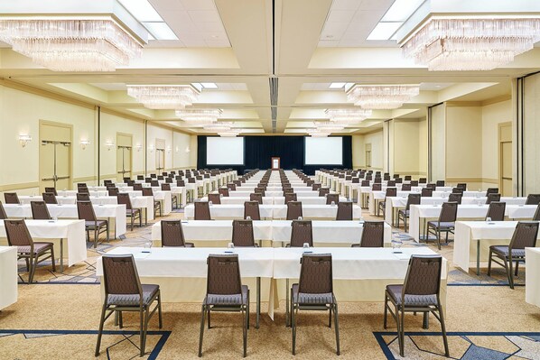 A large conference room with rows of tables and chairs, a stage, and a large screen.