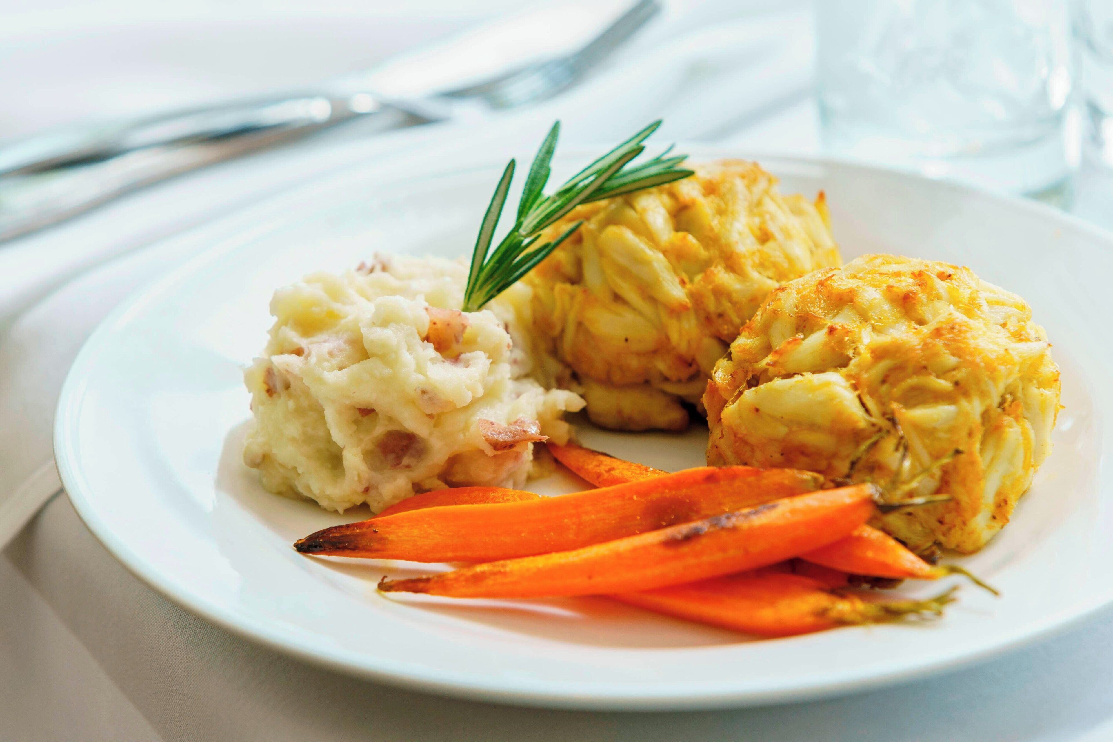 A plate with mashed potatoes, roasted carrots, and a baked dish, garnished with a sprig of rosemary.