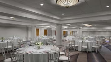 A spacious banquet hall with round tables, chairs, and elegant lighting fixtures.