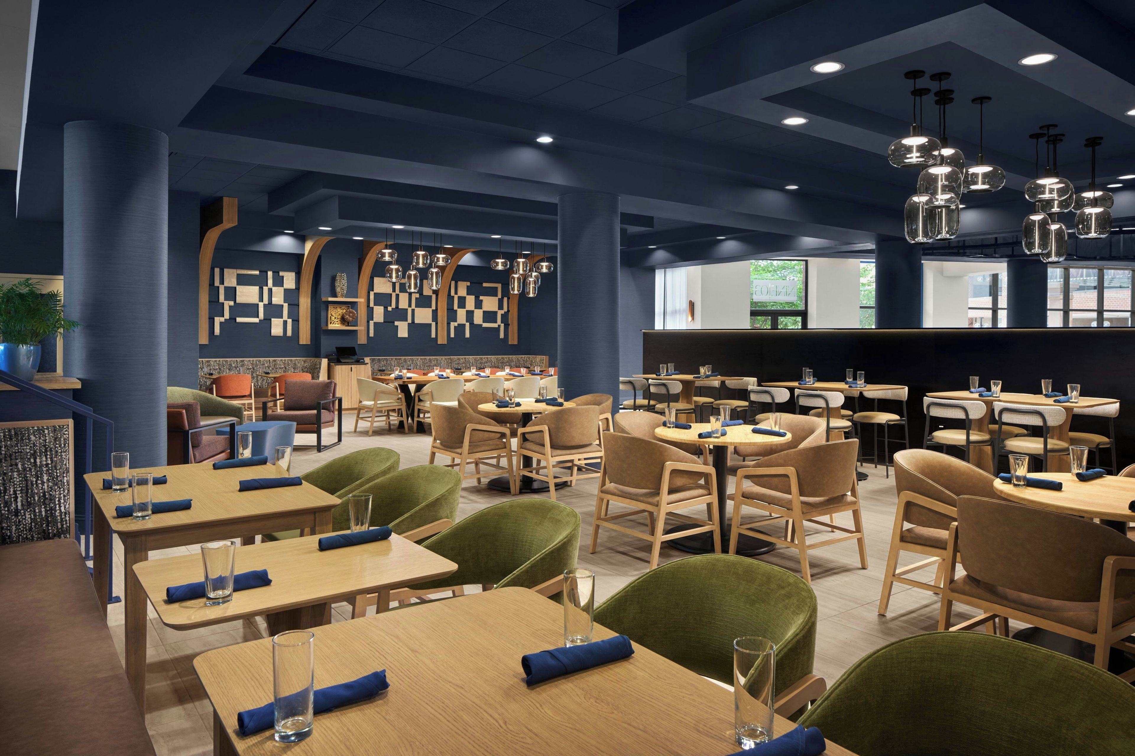 A modern restaurant interior with multiple dining tables and chairs, a bar area, and decorative wall art.