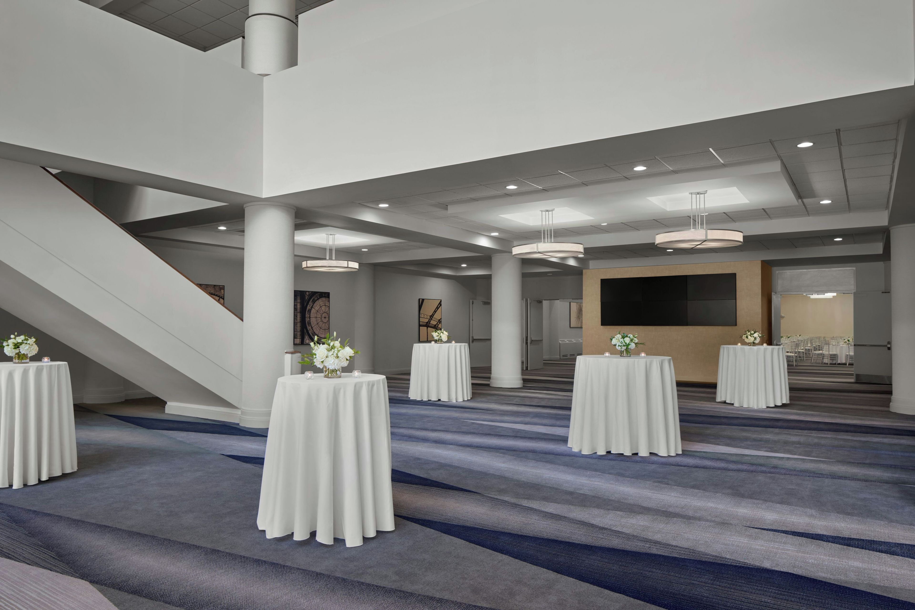 Una amplia sala de conferencias con techos altos, varias mesas con manteles blancos y piso alfombrado.