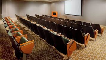 A conference room with rows of chairs, a projector screen, and a podium.